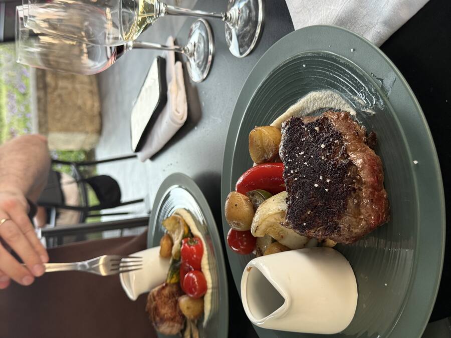 A seared steak with vegetables and a pitcher of cream sauce